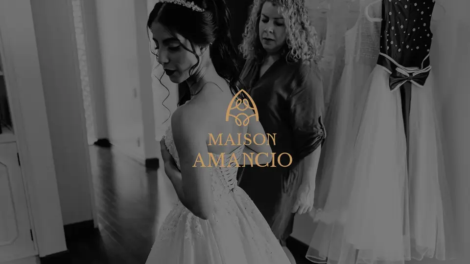 Logotipo dourado da Maison Amancio sobre foto em preto e branco de uma noiva entre vestidos do ateliê.