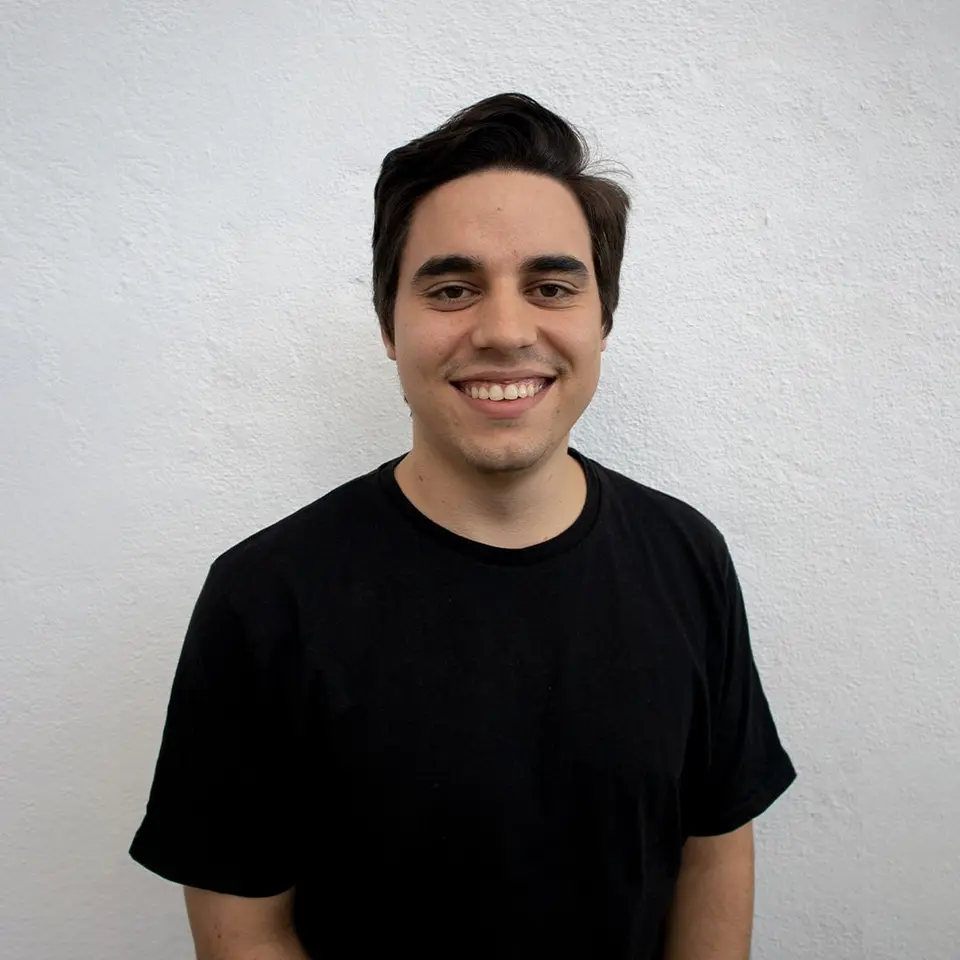 Retrato de Victor Arias, de camiseta preta, sorrindo diante de uma parede branca.